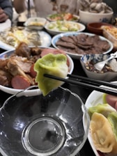 A colorful spread of traditional Chinese dishes including mapo tofu, dumplings, bao buns, and a bowl of noodles on a rustic wooden table