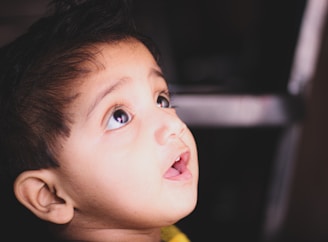 A child looking upwards with an expression of wonder, capturing the soft lighting on their face and open mouth. Their eyes are wide, and their hair is neatly styled.