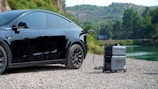 A compact portable EV charger plugged into a car during a scenic mountain camping trip