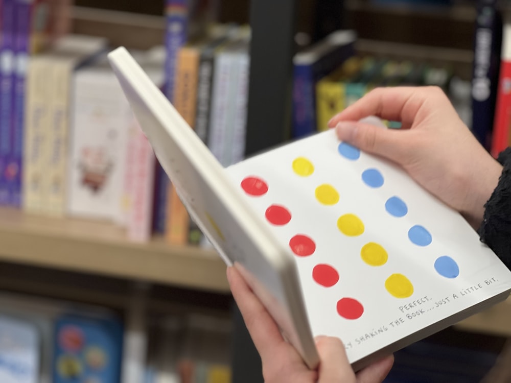 a person holding a book in front of a book shelf