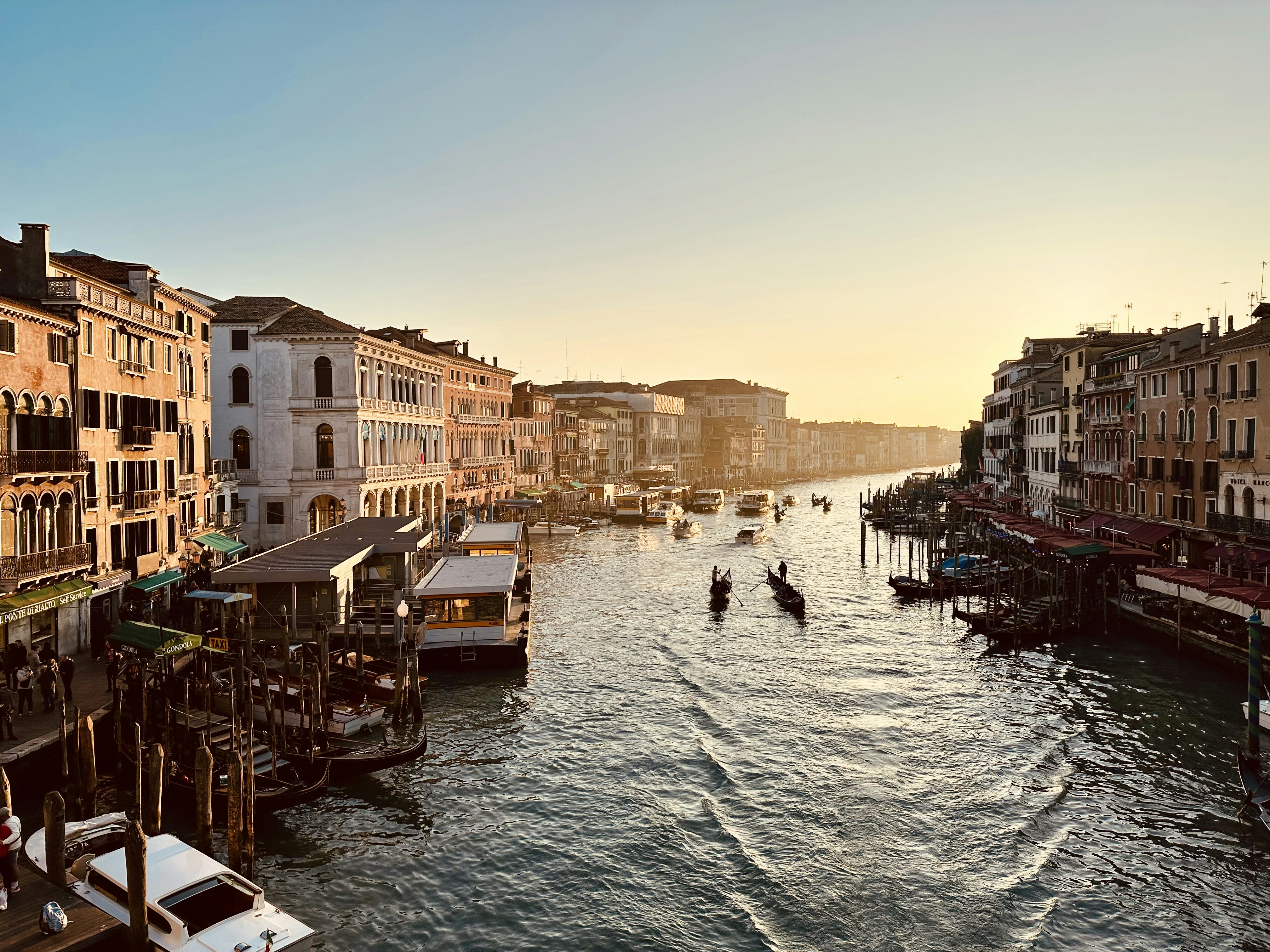 Venice grand canal at golden hour, colorful historic buildings, gondolas on shimmering amber water, warm sunset light