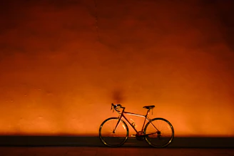 Bright orange road bike leaning against a white wall with clean shadows, embodying minimalism and simplicity.