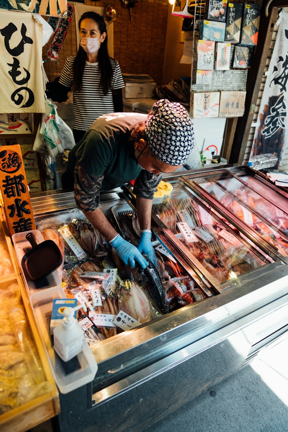 a man wearing a mask and gloves is looking at meat in a market