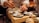 A chef is carefully plating a dish with precision, using chopsticks to add garnish on small plates with meticulously arranged food. The setting is a warm, dimly lit kitchen, suggesting an intimate dining experience.