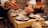 A chef is carefully plating a dish with precision, using chopsticks to add garnish on small plates with meticulously arranged food. The setting is a warm, dimly lit kitchen, suggesting an intimate dining experience.