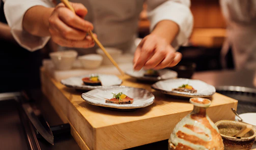 A cinematic shot of a chef plating a gourmet dish under warm, moody lighting in a stylish restaurant kitchen.