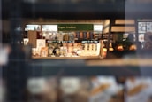 A store shelf filled with various packaged snacks and paper products. The foreground contains bags and cans, while in the background, shelves hold a variety of items including boxed cereals and napkins. Shoppers can be seen in the aisle beyond the shelves.