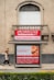 A street advertisement is placed in front of a stone building with an arched window. The ad promotes a website, marcobeteta.com, and suggests finding restaurants. It lists various cuisines such as Mexican, Israeli, Greek, and more, with an image of food including pasta and what appears to be shrimp.