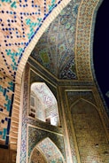 Intricate Islamic architectural details featuring colorful geometric patterns and calligraphy. The walls and ceiling are adorned with vibrant mosaics in shades of blue, turquoise, and gold, creating an ornate and mesmerizing effect.