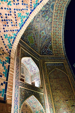 Intricate Islamic architectural details featuring colorful geometric patterns and calligraphy. The walls and ceiling are adorned with vibrant mosaics in shades of blue, turquoise, and gold, creating an ornate and mesmerizing effect.