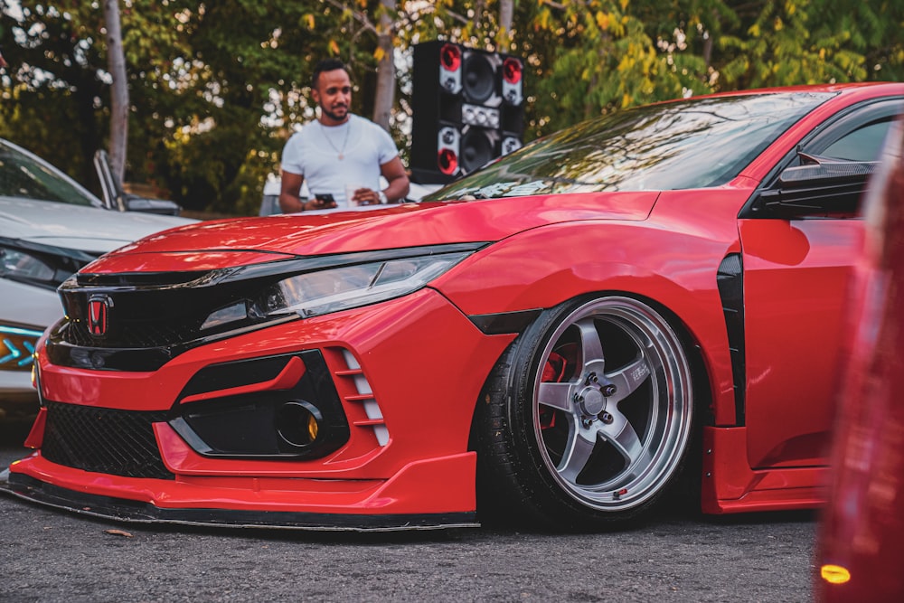 a red car parked in a parking lot next to a man