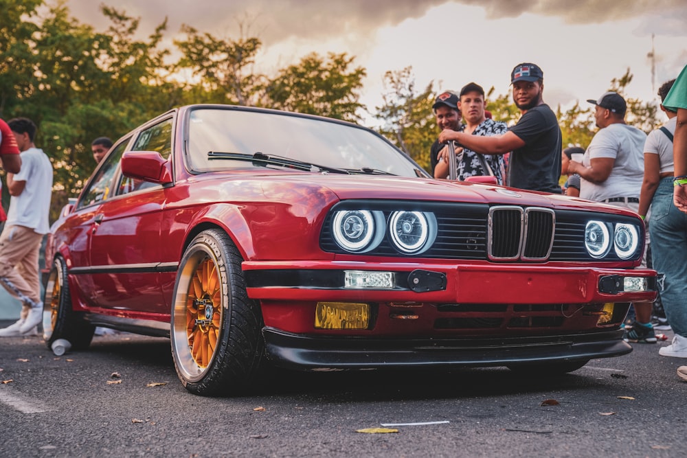 a group of people standing around a red car