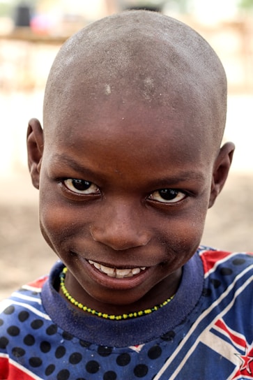 A child smiling gently while wearing a handmade wig called 'Baruqat al-Amal' symbolizing hope and courage.