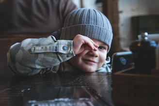 a young boy sitting at a table with his hands on his face
