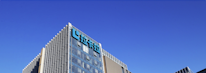 A modern office building with glass walls reflecting the clear blue sky. The structure has a prominent logo on the upper part, consisting of stylized blue letters.