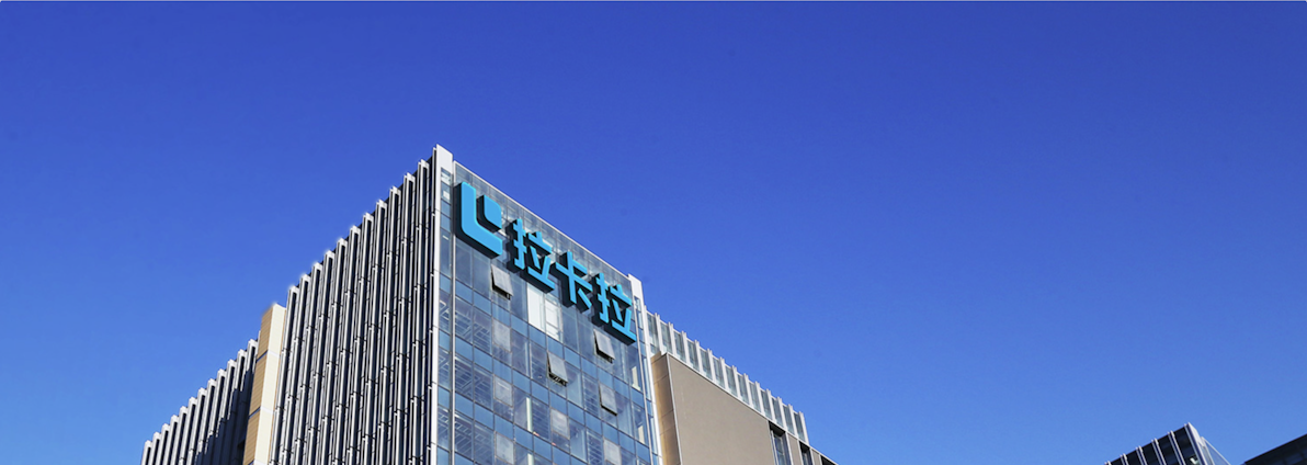 A modern office building with glass walls reflecting the clear blue sky. The structure has a prominent logo on the upper part, consisting of stylized blue letters.