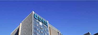 A modern office building with glass walls reflecting the clear blue sky. The structure has a prominent logo on the upper part, consisting of stylized blue letters.