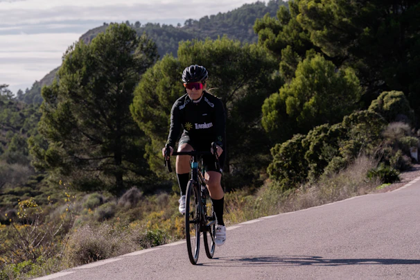 A content creator filming a cyclist wearing bright gear on a scenic countryside road.