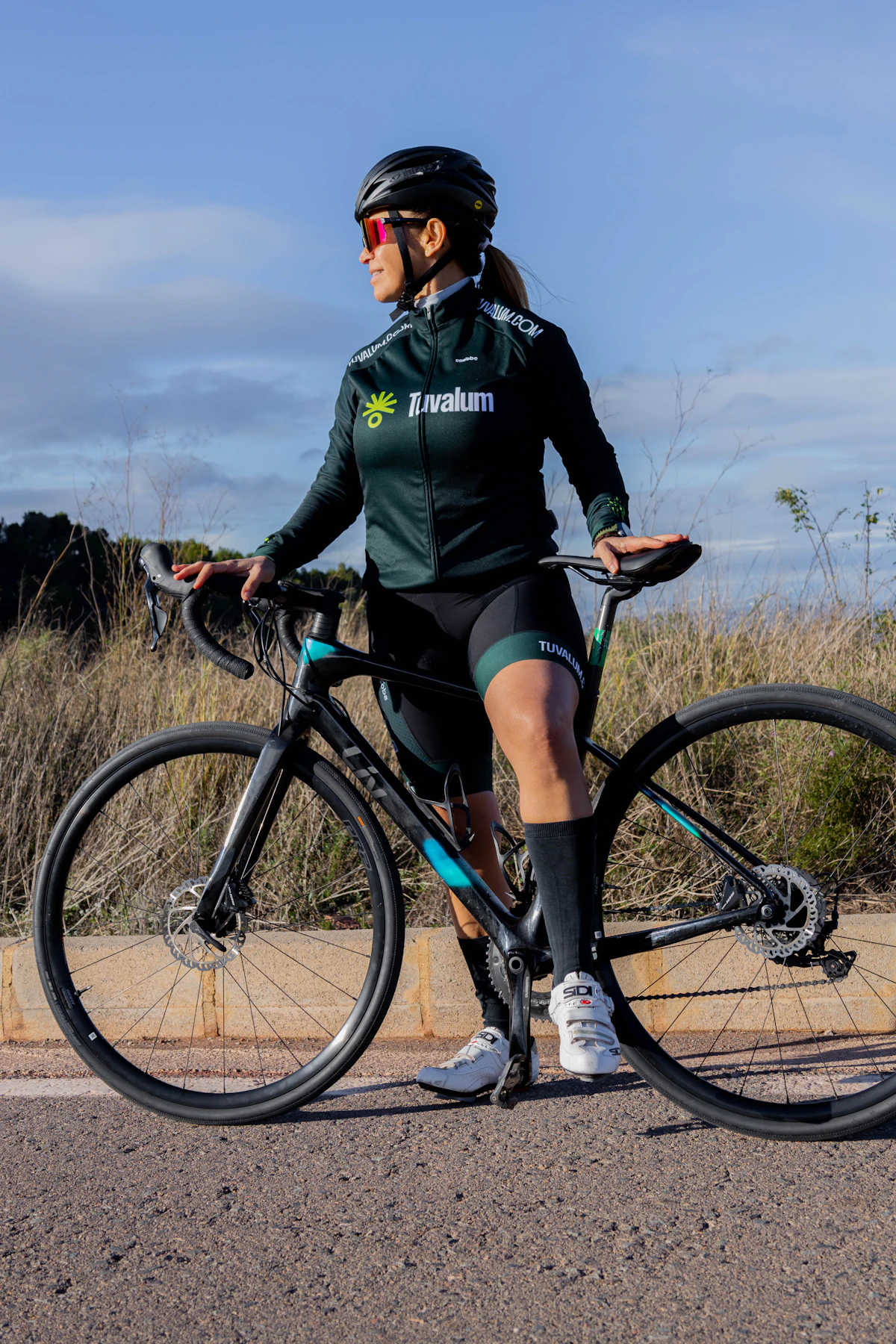 Una persona con casco permanece de pie junto a una bicicleta en el exterior.