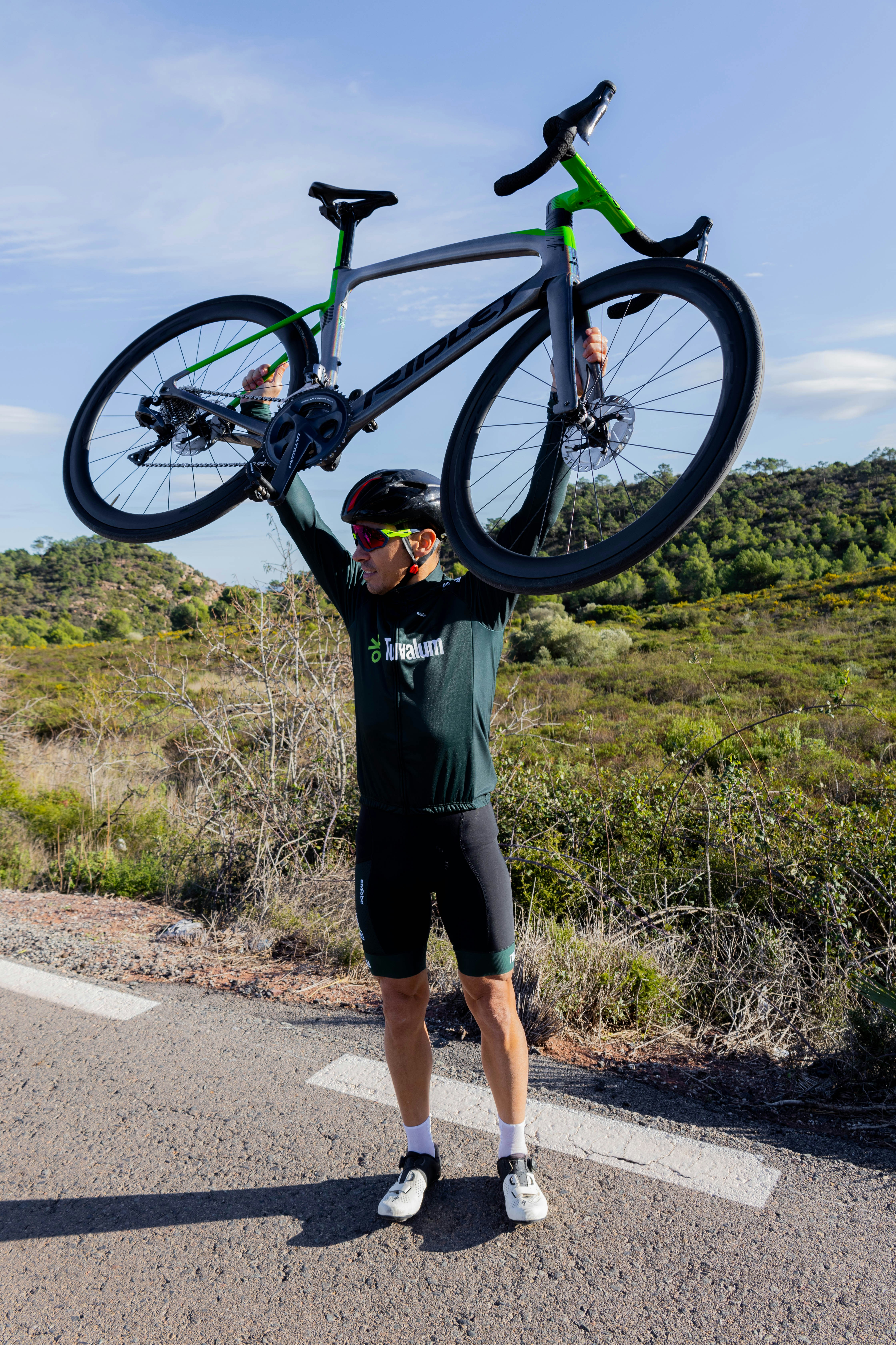 a man holding up a bike on the side of a road
