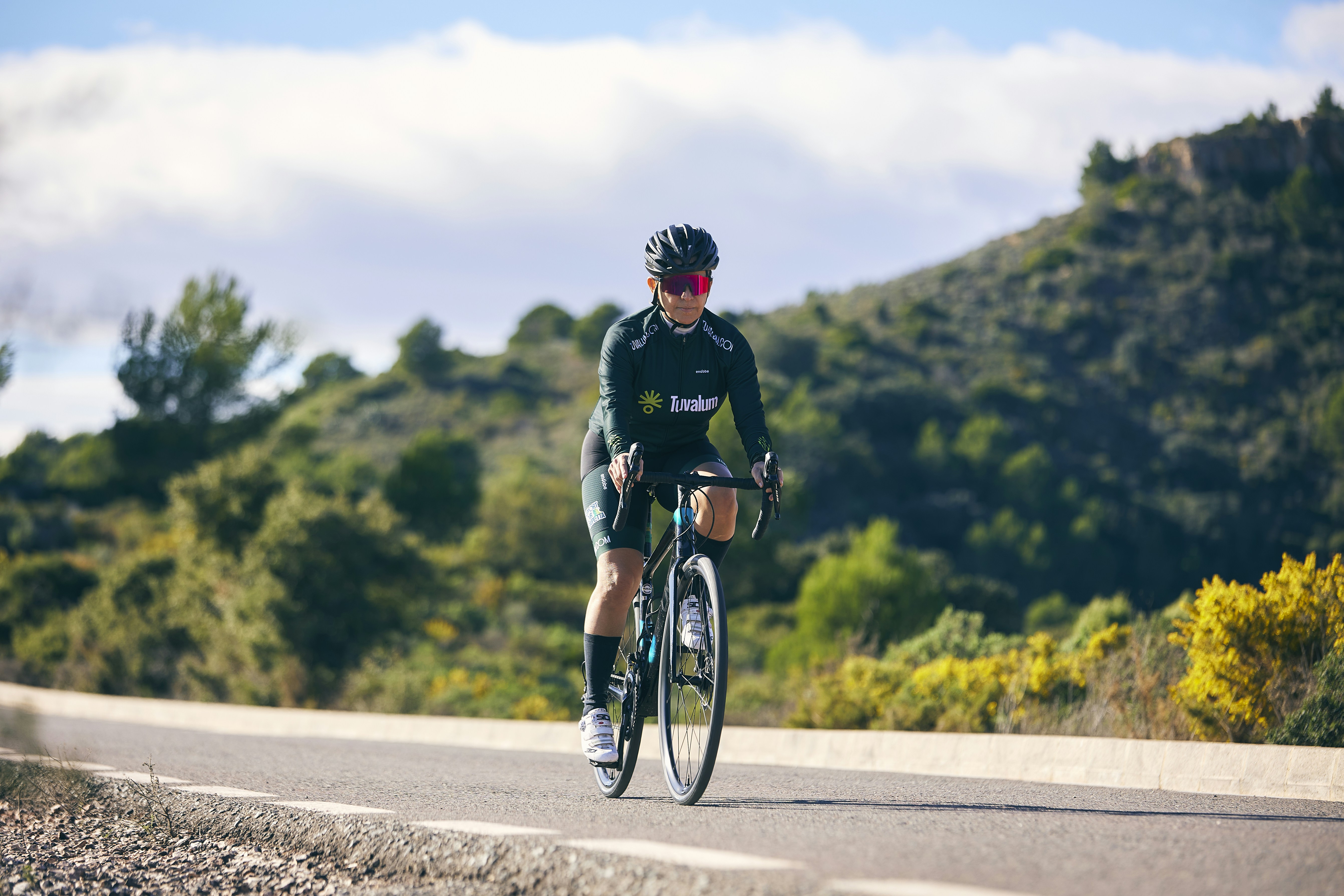 a man riding a bike down a road next to a lush green hillside