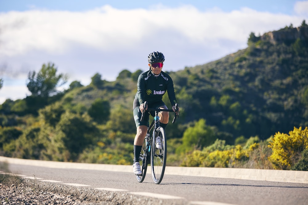 a man riding a bike down a road next to a lush green hillside