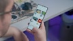 A person is holding and browsing a smartphone with a screen displaying a digital storefront or app interface. The background features a desk with a computer mouse and blurred elements, creating a tech-focused environment.