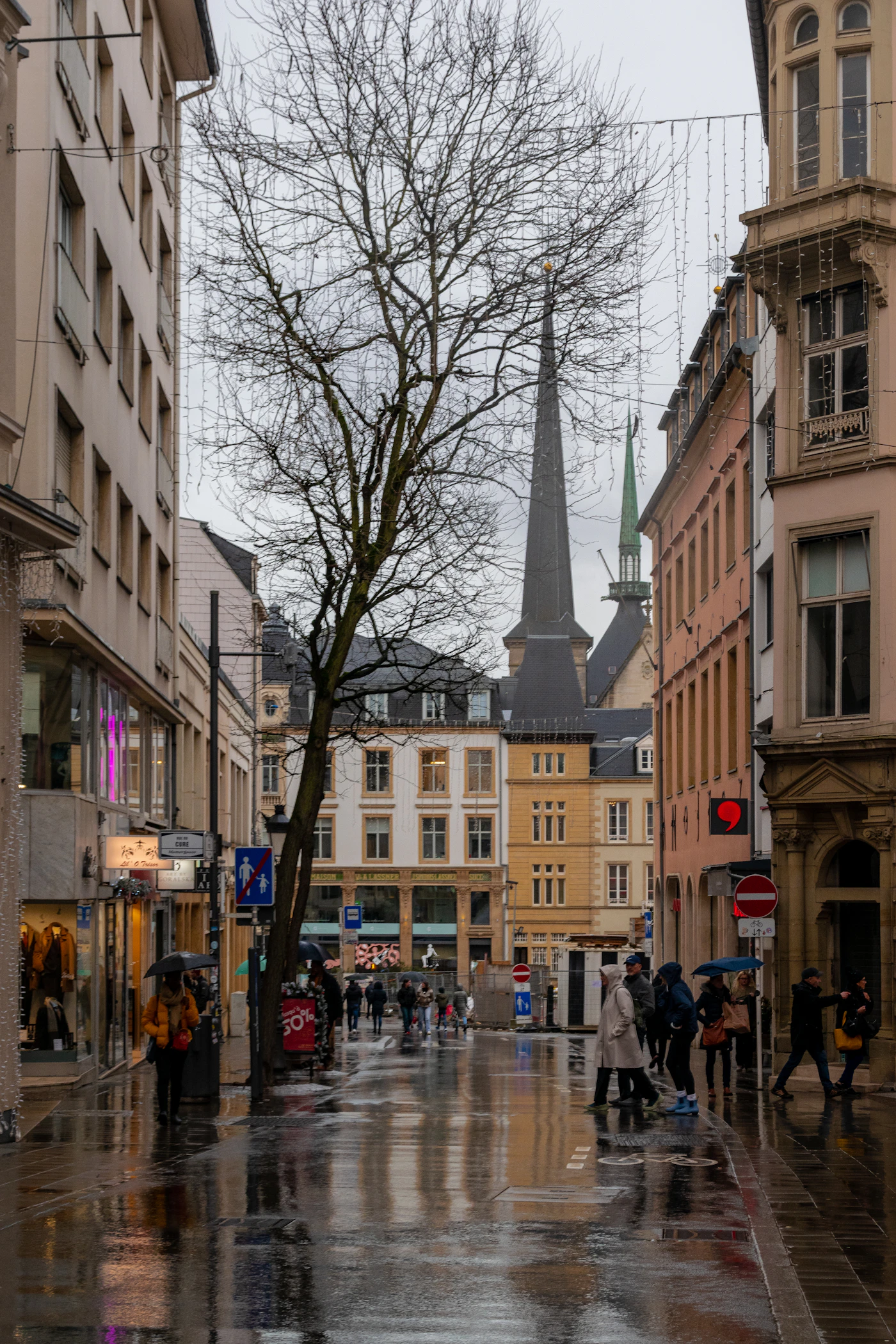 Street in a European city with a church steeple in the background and passers-by
