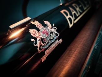 A close-up view of a black metallic object featuring an intricate crest emblem with a lion and unicorn, along with text that highlights the royal appointment to His Majesty King George. The adjacent area displays the partial letters 'BAR-L'.