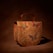 A leather handbag with intricate butterfly and floral designs, predominantly in shades of red, green, and purple. The background is a rich brown, giving a natural, earthy feel to the piece.