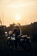 a person sitting on a motorcycle with the sun in the background