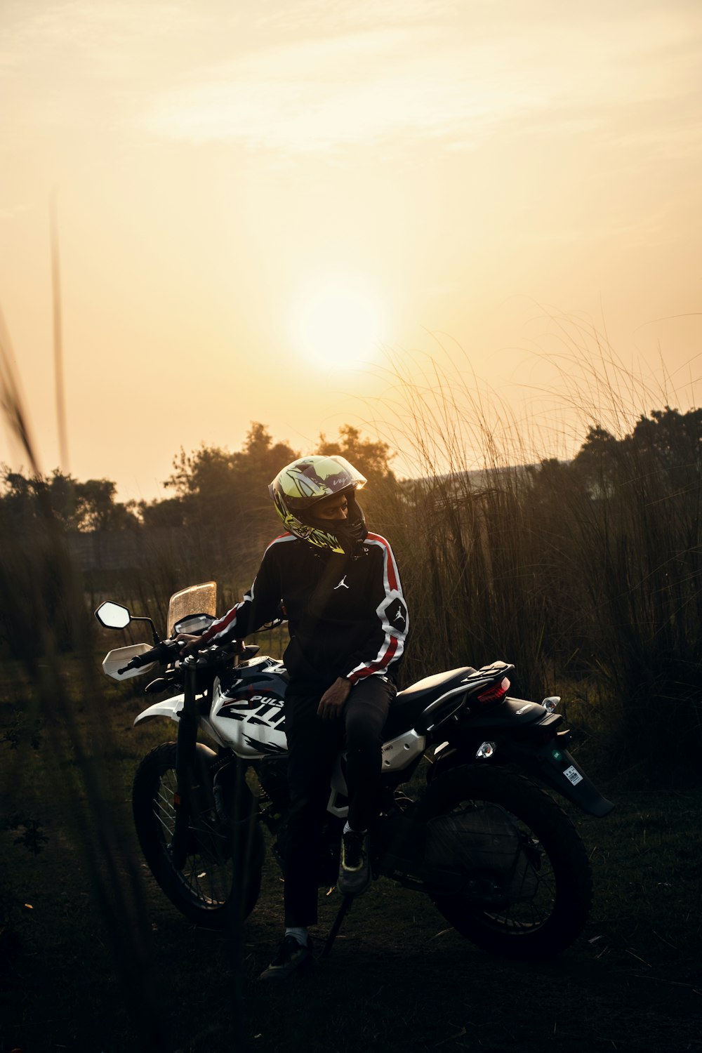 uma pessoa sentada em uma motocicleta com o sol ao fundo