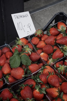A collection of ripe strawberries neatly arranged in plastic containers. A handwritten sign, in a language resembling Polish, indicates pricing or product information.