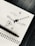 A geometric design is drawn on a white sheet of paper, featuring a central circle with various arrows, lines, and shapes extending outward. A black ink pen rests on the spiral binding of the notebook, which is placed on a dark wooden surface.