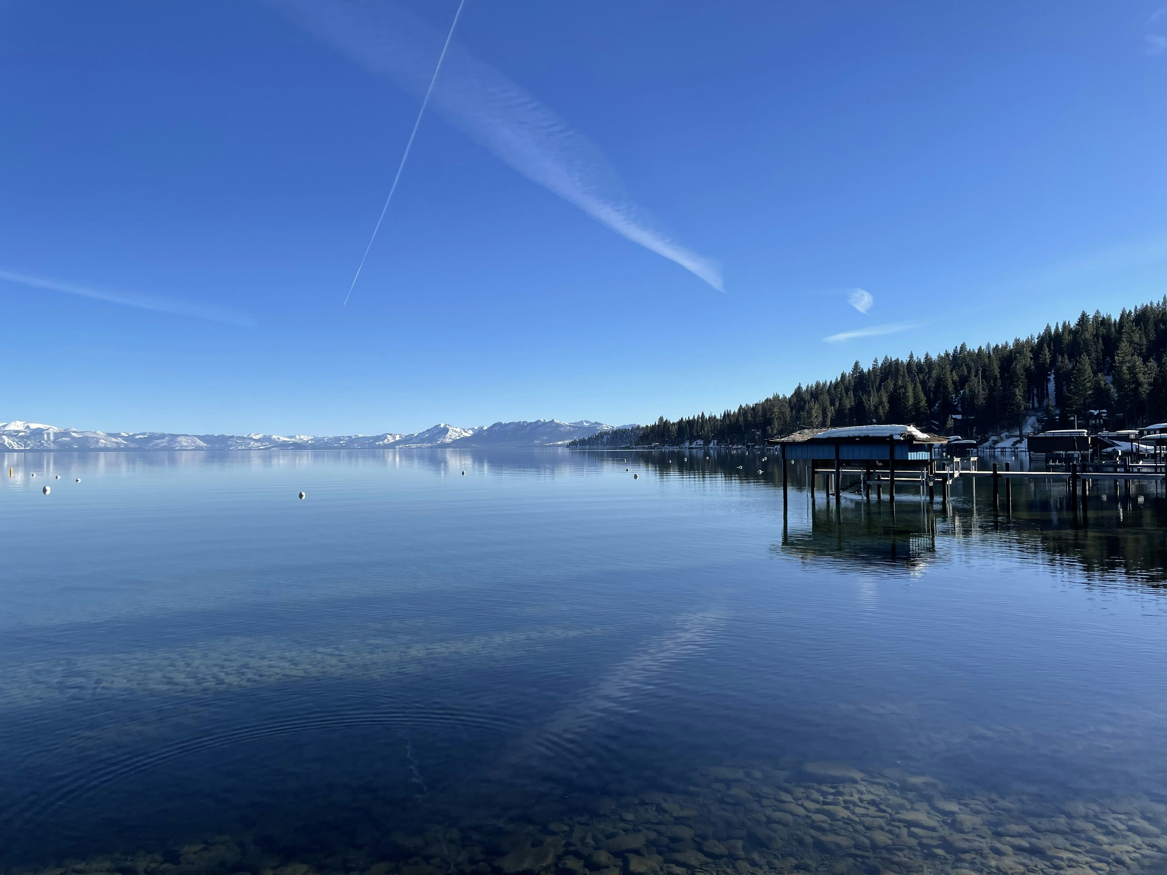Calm lake with a boathouse and distant snow-capped mountains.