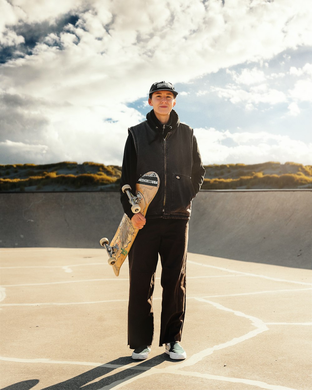 a man holding a skateboard standing in a parking lot