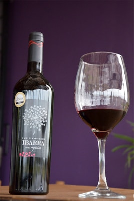 A bottle of wine labeled 'Familia Ibarra Vinos' is placed next to a filled wine glass. The background is a deep purple, adding contrast and elegance to the scene.