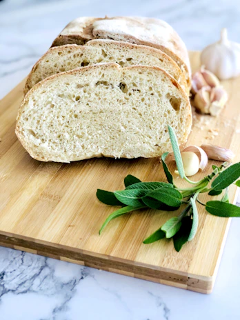 Hands arranging artisanal bread and fresh herbs on a wooden board, highlighting the textures and natural colors.
