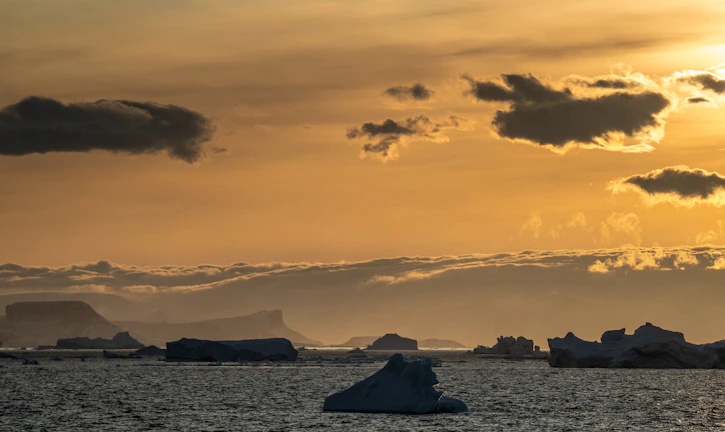 A serene polar sunrise casting golden light over icy waters beside a sleek expedition ship.
