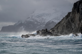 A rugged Greenland coastline with mining equipment near a port under a cloudy sky.