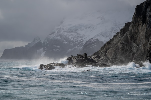 A rugged Greenland coastline with mining equipment near a port under a cloudy sky.