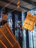 A series of golden metallic plates with engraved text hang from wires. They are set against a backdrop of blue, semi-transparent curtains with light filtering through, casting intricate shadows.