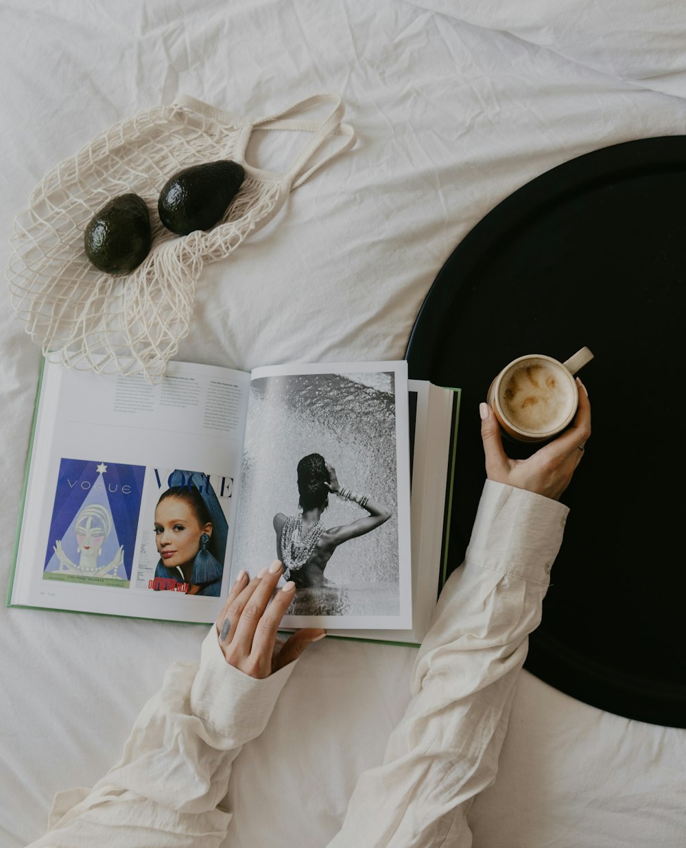 a person reading a book on a bed with a cup of coffee