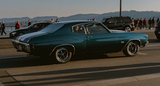 A shiny American muscle car displayed on a coastal road with mountains in the background.