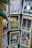 A collection of vintage-style postcards displayed on a rotating rack, featuring artistic illustrations and typography. Each postcard has a unique design and depicts different themes, such as landscapes, animals, and abstract art. The cards are displayed in metal holders attached to a wooden stand.