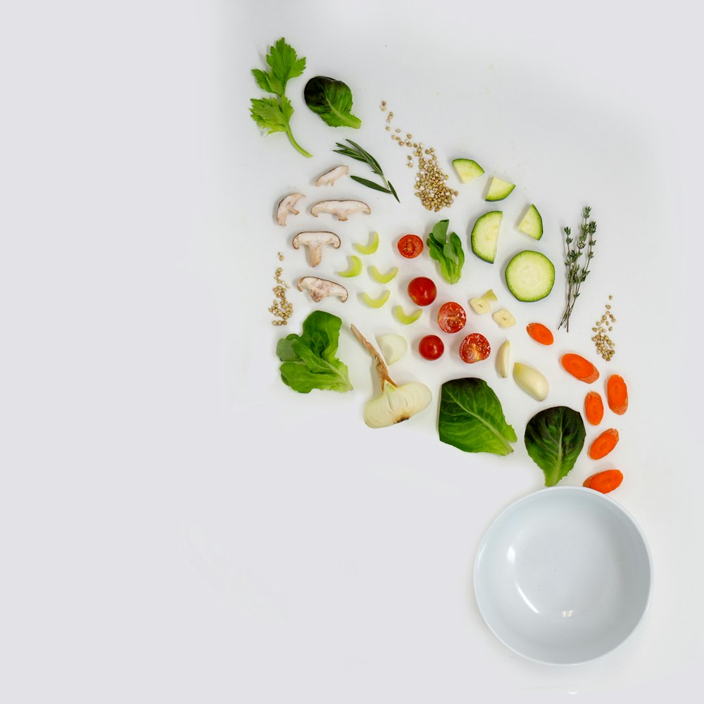 a white bowl filled with assorted veggies on top of a white table