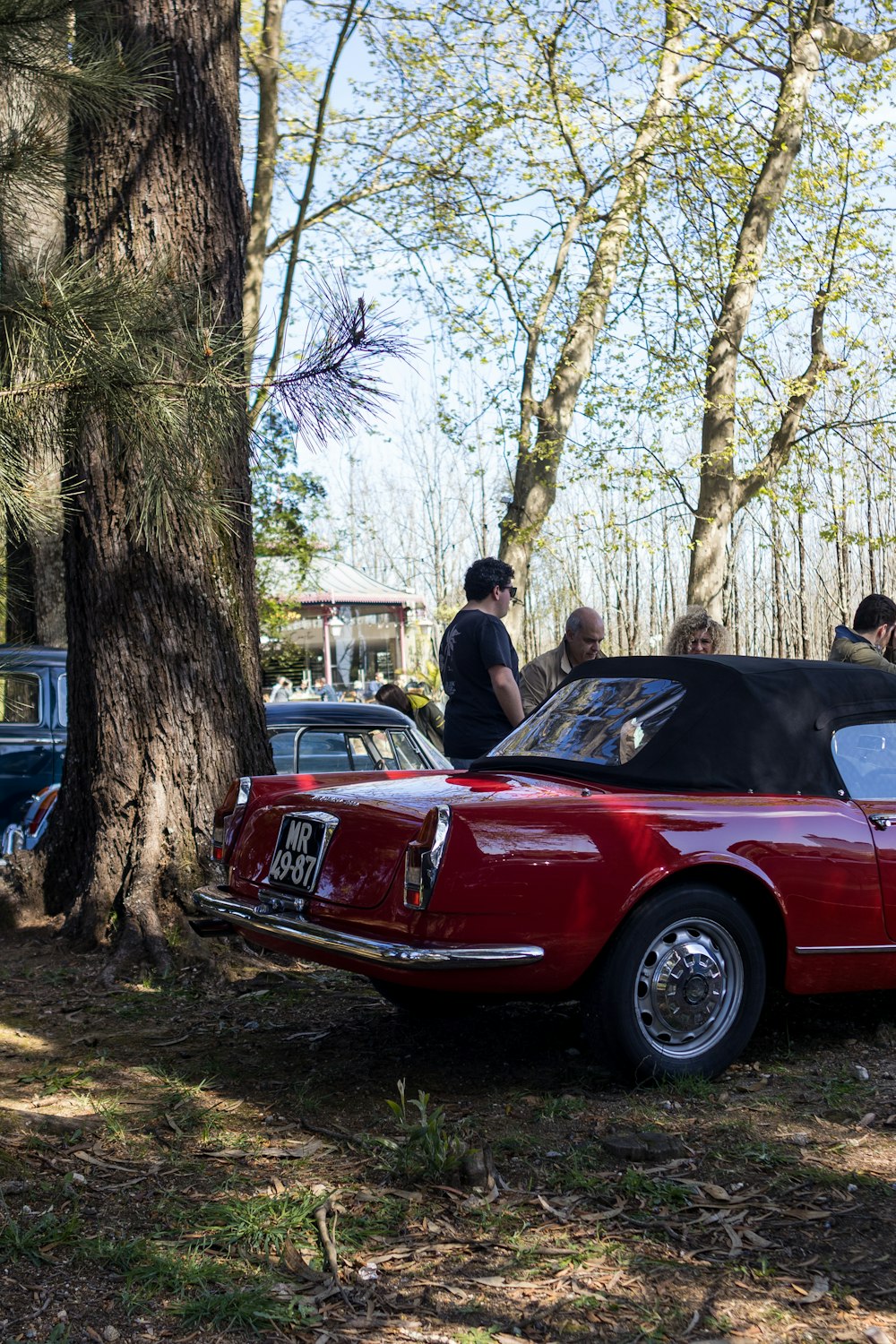 a group of people standing around a red car