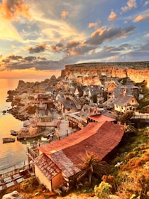 A charming coastal village with bright houses and a calm sea reflecting the sunset hues.