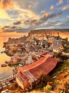 A charming coastal village with bright houses and a calm sea reflecting the sunset hues.