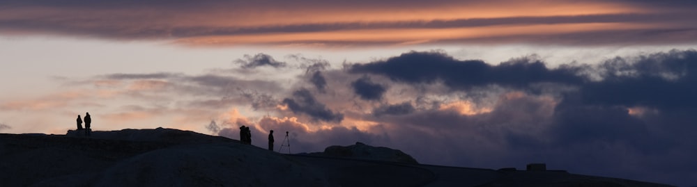 a group of people standing on top of a hill under a cloudy sky